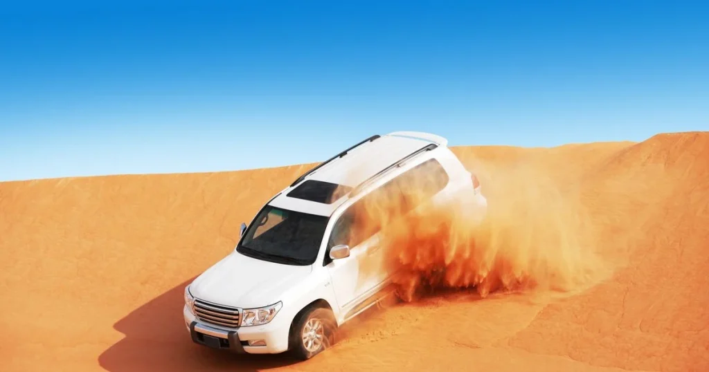 A 4x4 Land Cruiser performing dune bashing in the red dunes of Dubai during sunset.